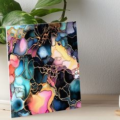 a colorful abstract painting on a white table next to a potted plant and vase