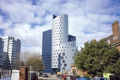 cars parked in front of tall buildings on a street with blue sky and white clouds