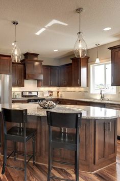 a large kitchen with wooden floors and dark wood cabinets, two bar stools at the center island