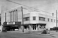 an old black and white photo of a movie theater with cars parked in front of it