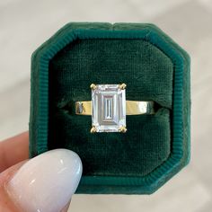 someone is holding an emerald colored ring with a diamond in it's middle finger