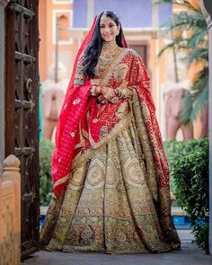 a woman in a red and gold bridal gown standing outside an archway with her hand on her hip