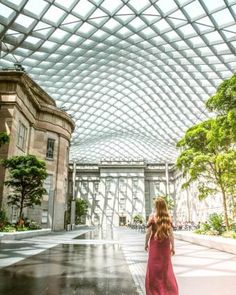 a woman in a red dress is walking through an indoor building with a glass roof