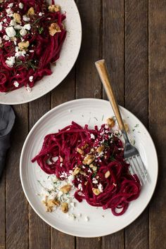 two white plates topped with red pasta and garnished with fettuccine