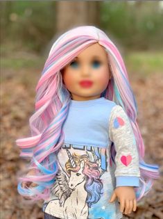 a doll with pink and blue hair is standing in the leaves, wearing a t - shirt with an unicorn on it