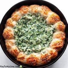 a pizza with spinach and cheese in a black skillet on a white surface