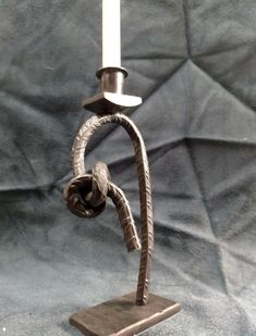 a metal candle holder with a single white candle on it's end and a twisted handle