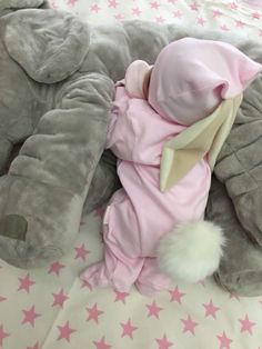 a baby in a pink outfit laying on top of an elephant stuffed animal bedding