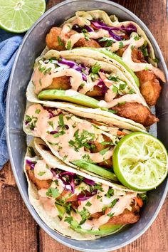 fish tacos in a bowl with lime wedges on the side