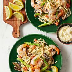 two green plates topped with shrimp and pasta next to lemon wedges on a cutting board