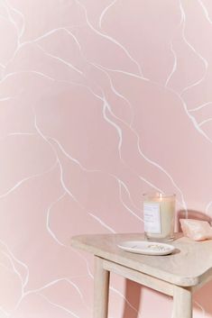 a table with a candle on it in front of a wallpapered pink background