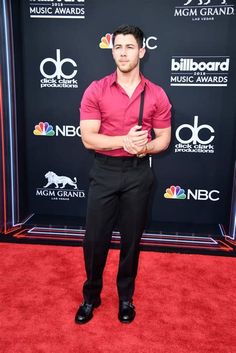 a man in a pink shirt and black pants on the red carpet at an awards event