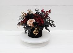 a black vase with red and pink flowers in it on a white plate against a white background