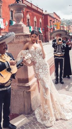 a woman in a wedding dress standing next to a man with a guitar and other musicians