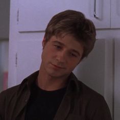 a young man standing in front of a white refrigerator with his eyes closed and looking at the camera