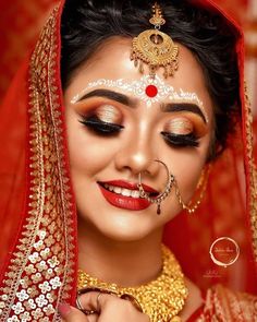 a woman with makeup on her face and red veil over her head, wearing gold jewelry