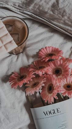 pink flowers are in a vase next to a book and some ice cubes on a bed