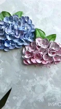 two blue and pink flowers sitting on top of a white table next to a pair of scissors