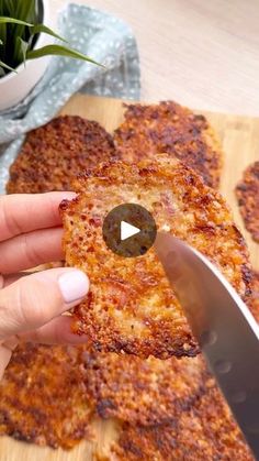 a person cutting pizza with a knife on a wooden board next to a potted plant