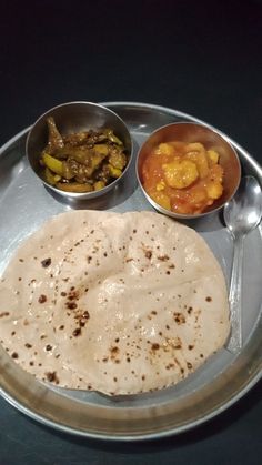 a metal plate topped with different types of food on top of a black table next to silver spoons