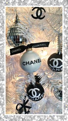 chanel ornaments hanging on a white christmas tree with black and silver decorations around them