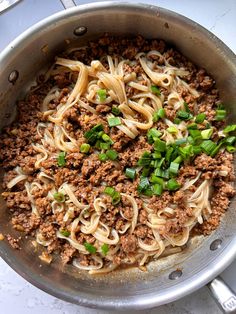 a pan filled with noodles, meat and green onions