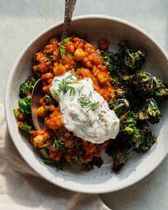 a white bowl filled with lots of food on top of a table next to a spoon