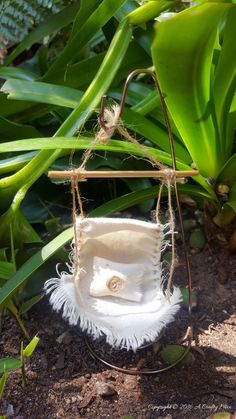 a white purse hanging from a tree branch in the grass with some plants behind it