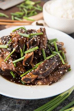 a white plate topped with meat covered in sesame seeds and garnished with green onions