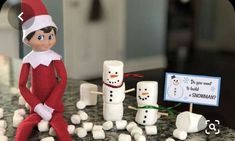 an elf sitting on top of a counter next to marshmallows and snowmen