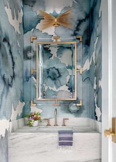 a bathroom with blue and white wallpaper, gold fixtures and a mirror above the sink