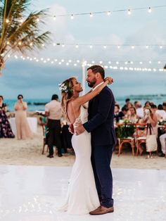 a bride and groom share their first dance on the beach in front of an audience