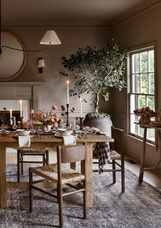 a dining room table and chairs with candles on the tables in front of them, next to a potted tree