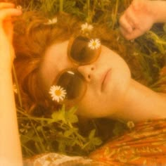 a woman laying in the grass with her eyes closed and daisies pinned to her hair