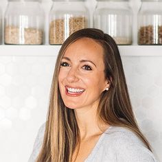 a smiling woman standing in front of jars filled with grains and cereals on shelves