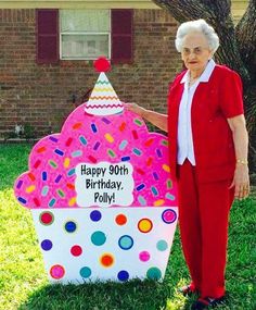 an older woman standing in front of a giant cupcake shaped birthday cake with sprinkles