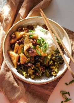 a bowl filled with rice, broccoli and tofu next to chopsticks