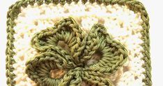 a crocheted square with a green flower on the center and white yarn in the middle