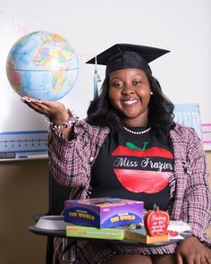 a woman sitting in a chair holding up a globe and wearing a black shirt with an apple on it