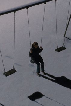 a person sitting on a swing set in the snow with their shadow cast by them