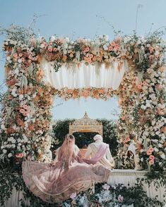 a bride and groom are sitting under an archway decorated with flowers