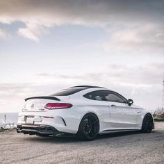 the rear end of a white car parked on top of a gravel road next to the ocean