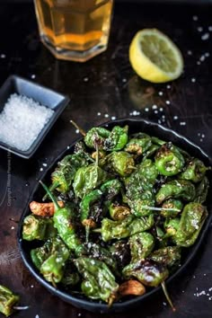 a pan filled with cooked green peppers next to a glass of water and lemon wedges