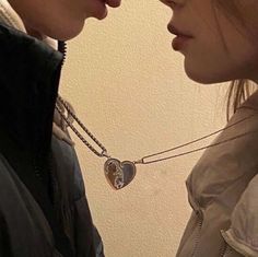 two people standing next to each other and one has a heart shaped pendant on it