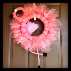 a pink flamingo wreath hanging on the front door with a heart shaped candle in it