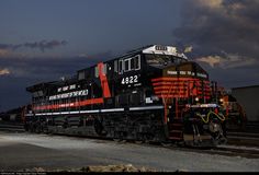 a black and red train traveling down tracks under a cloudy sky with clouds in the background