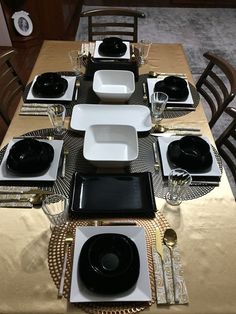 the table is set with black and white plates, silverware, and gold napkins