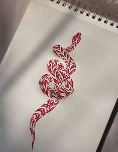 a spiral notebook with a red and white snake on the cover next to a pen