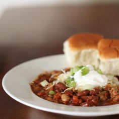 a white plate topped with a sandwich and beans covered in sour cream on top of a wooden table