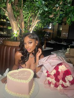 a woman sitting at a table with a cake in front of her and flowers on the table